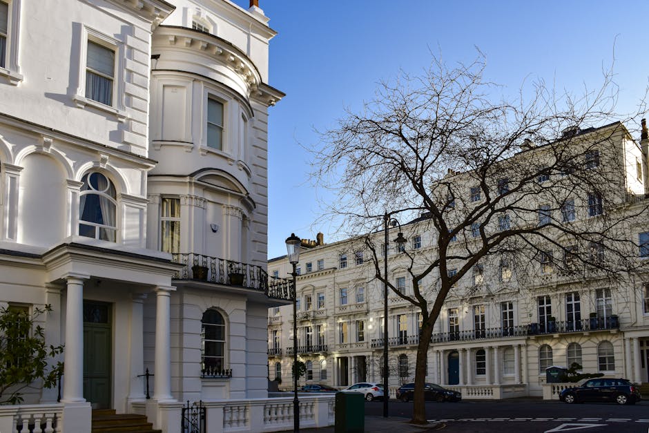 A multi-storey white building with classical architectural features, including decorative columns, ornate window surrounds, and a balustrade balcony on the upper floors, situated on a paved street wit