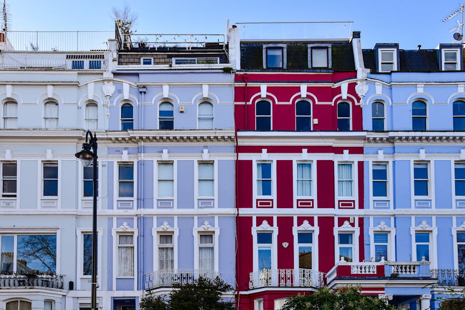 This image shows the exterior of a row of multi-story residential buildings in Primrose Hill, featuring a light blue facade with decorative architectural details and bay windows. The street is lined w