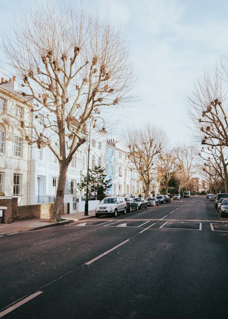An expansive view of Regent's Park in London on a bright, sunny day, with numerous visitors sitting on the grass and walking along the pathways. The park features lush green lawns, scattered trees, an